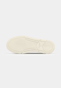 Rubber sneaker sole in off-white with a textured herringbone pattern and defined grooves, featuring subtle branding near the heel.