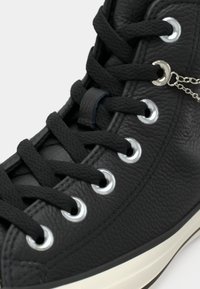 Sneaker alta in pelle nera con parte superiore testurizzata, occhielli argento e lacci neri. Accento di catena argento notevole vicino all'occhiello.