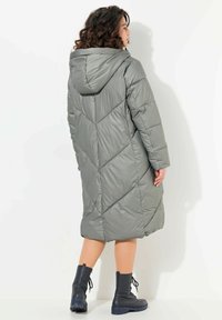 Cappotto grigio imbottito e con cappuccio, dalla silhouette lunga, caratterizzato da un motivo a quadri geometrico e indossato sopra stivali alla caviglia neri con lacci.