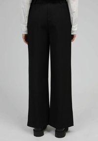 Pantalons larges noirs en tissu lisse, dotés d'une taille haute et d'un design épuré sans motifs ni embellissements visibles.