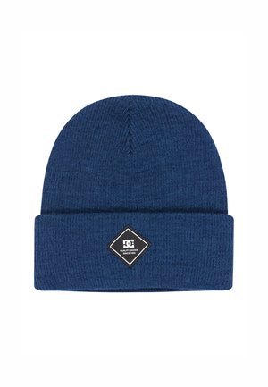 Blauwe gebreide muts met een omgeslagen boord, voorzien van een zwart diamantvormig label met wit logo en tekst. Gemaakt van een zachte, gestructureerde stof.