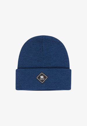 Blauer Strickmütze mit umgeschlagenem Bündchen, versehen mit einem schwarzen, rautenförmigen Aufnäher mit weißem Logo und Text. Hergestellt aus einem weichen, strukturierten Stoff.