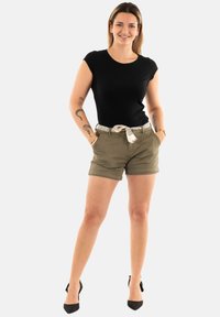 T-shirt noir ajusté, shorts vert olive avec des ourlets retroussés et une ceinture à motifs. Des talons hauts noirs complètent l'ensemble.