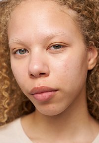 Close-up of a face with light skin, curly blonde hair, and natural makeup. Features visible include freckles, a smooth complexion, and light makeup on lips.