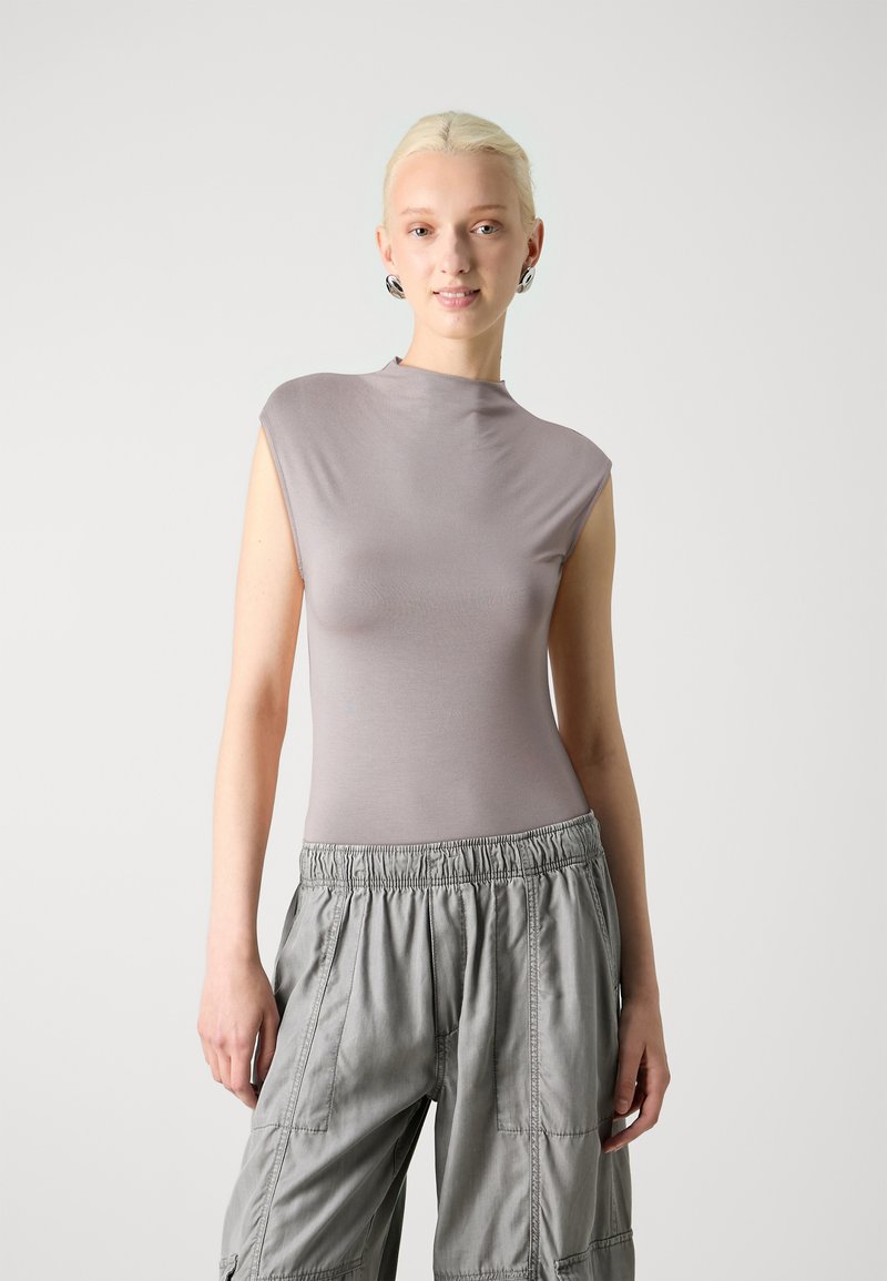 Sleeveless, fitted top in light lavender with a high neck. Worn with loose, gray cargo pants featuring an elastic waistband and pockets.