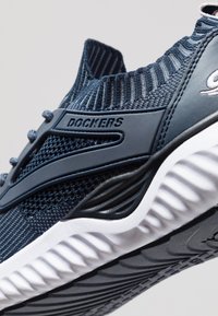 Primo piano di una sneaker Dockers blu navy con tessuto a maglia, suola in gomma e colletto alla caviglia a coste.