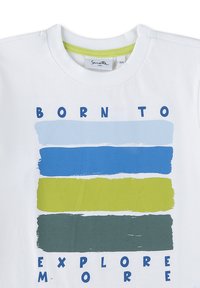 Weißes Shirt mit dem Text "Born to Explore More" und vier horizontalen Farbstreifen in Hellblau, Blau, Gelbgrün und Dunkelgrün.