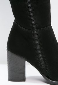 Stivale alla caviglia in suede nero con tacco a blocco, dotato di zip laterale, texture liscia e design aderente che si adatta alla gamba.