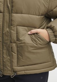 Olive green puffer jacket with a diamond quilted design, featuring a side pocket and elastic cuffs for a snug fit. Smooth, synthetic material.