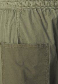 Olivgröna shorts med elastisk midja, som har en ficka med applikation. Lätt material med en något strukturerad yta.