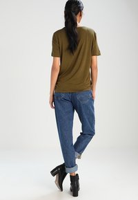T-shirt verde oliva abbinato a jeans in denim blu rilassati. Stivali neri alla caviglia con tacco chunky. Design semplice e informale.