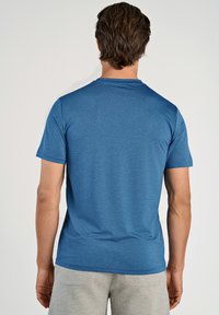 Blå kortärmad t-shirt i texturerad stickad tyg med rund hals, kombinerad med grå shorts. Vy bakifrån som visar ren sömnad.