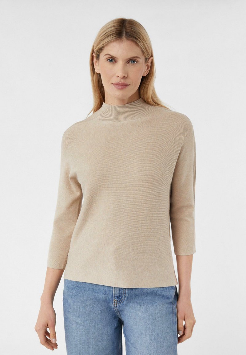 Beige ribbel gebreide trui met een hoge nek en driekwartmouwen, gecombineerd met lichtblauwe denim jeans. Eenvoudig en schoon ontwerp.