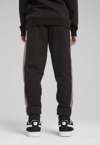 Pantalons de survêtement noirs avec des rayures grises sur les côtés, dotés d'une coupe décontractée et d'une taille élastique, associés à des baskets noires et blanches.