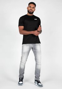 Sort kortærmet t-shirt med hvidt logo, parret med lysegrå slim-fit jeans og sort-hvide højtop sneakers.