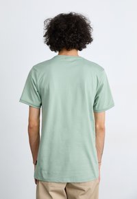 Lys grønne bomuld t-shirt med rund hals og korte ærmer, der viser en glat tekstur. På bagsiden er der et lille sort label nær kanten.