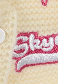 Knitted cream fabric with a soft texture. Features pink and white embroidered text for "Skye." Includes a white button detail.