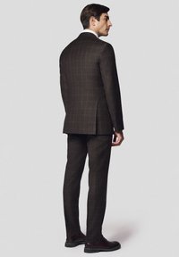 Ciemnobrązowy garnitur w kratę o dopasowanym fasonie. Zawiera jeden wentyl z tyłu i jest zestawiony z brązowymi butami.