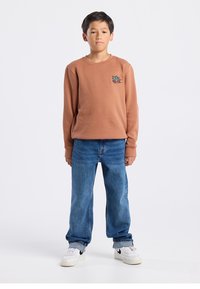 Brown sweatshirt with embroidered colorful design, paired with blue straight-leg jeans and white sneakers with black accents.