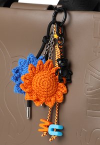 Bruine tas van nep leer met kleurrijke gehaakte bloem sleutelhangers in blauw en oranje, zwarte berenhanger en levendige plastic letters.