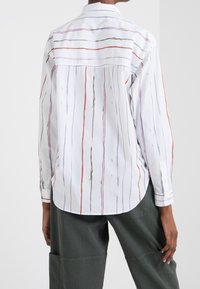 Witte button-up blouse met verticale meerkleurige strepen en een afgeronde zoom. Gemaakt van lichtgewicht stof met lange mouwen en een kraag.