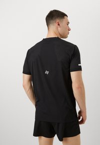 Svart treningst-skjorte med et teksturert mønster med små perforeringer, rund hals og en logo på baksiden, kombinert med svarte shorts.