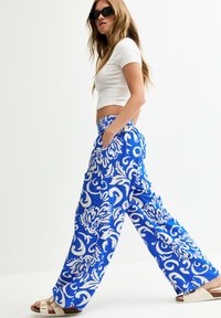 Pantalons larges à motifs bleus et blancs avec un design floral, présentant une coupe décontractée et des poches latérales, associés à un haut court blanc.