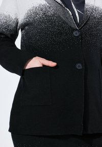 Musta ja harmaa ombre-takki, jossa on teksturoitu kangas, kaksi nappia ja etutasku. Täydellinen viimeistely tonalisella gradienttikuvioilla.