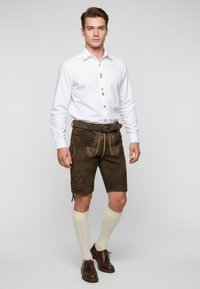 Hnědé kožené šortky se zdobným stehem, bílé tričko s vertikálními detaily, krémové podkolenky a hnědé boty.