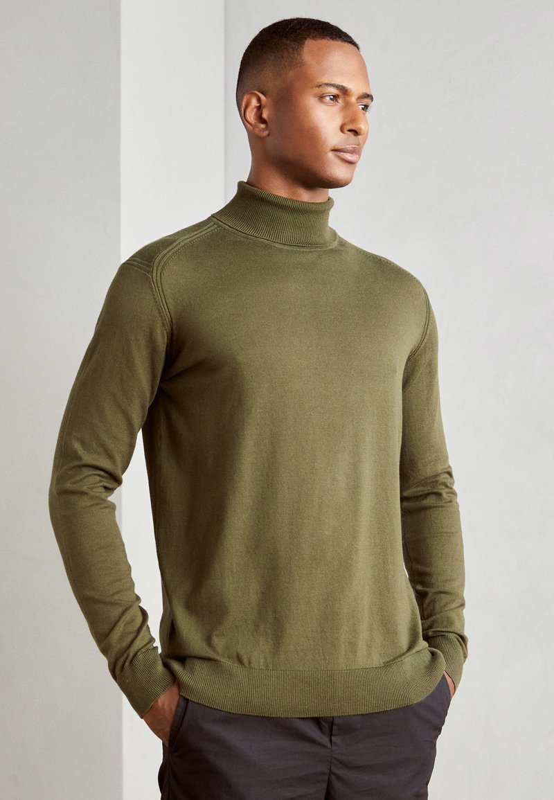 Maglione a collo alto verde oliva realizzato in tessuto morbido, con polsini e orlo a costine, silhouette aderente e maniche lunghe.