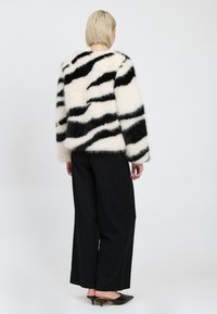 Pelsagtig sort og hvidstribet sweater med en blød tekstur, parret med brede sorte bukser og sorte spidse hæle.