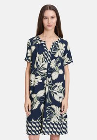 Námořnické květinové šaty z měkkého materiálu; mají krátké rukávy, výstřih do V a bílé květinové vzory s vlnitým lemováním.