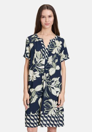 Marineblaues Blumenkleid aus weichem Stoff; mit kurzen Ärmeln, V-Ausschnitt und weißen Blumenmustern sowie einem wellenförmigen Saumdetail.