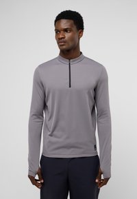Langemouw, lichtgrijze pullover met een kwart-rits en een staande kraag. Heeft een getailleerd ontwerp en gladde, textuurstof.