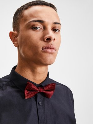 Pajarita roja con textura llevada sobre una camisa negra, con una forma clásica y un diseño sutil que realza la apariencia formal.