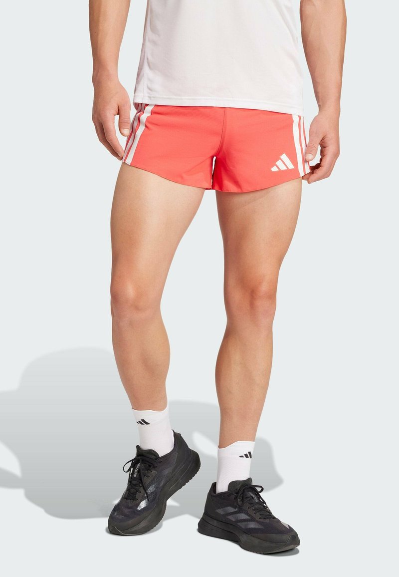 Koraalrode sportshorts met witte zijstrepen, lichtgewicht stof, elastische tailleband. Draagt met zwarte sneakers en witte sokken met merklogo.