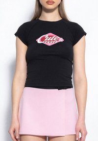 Czarna koszulka z krótkim rękawem z różowym nadrukiem "Cute & Tasty" z przodu, zestawiona z dopasowaną różową spódnicą. Gładka faktura materiału.