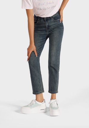Jeans in denim scuro con una vestibilità a gamba dritta, caratterizzati da una vita alta e cuciture minimali. Abbinati a sneakers platform bianche con accenti verde menta.