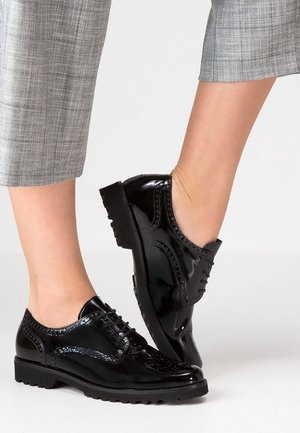Czarne lakierowane buty ze skóry z ozdobnym wzorem brogue, z perforacjami dekoracyjnymi i masywną podeszwą, zestawione z szarą, kratowaną spodnią.