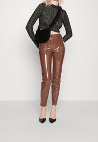 Hnědé lesklé, těsně padnoucí kalhoty s lesklou texturou, spárované s černým zkráceným žebrovaným svetrem a malou černou kabelkou na rameno.