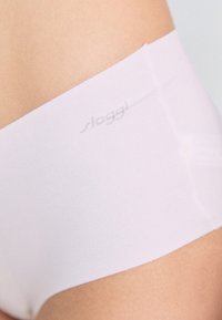 Svijetloružičasto nevidljivo donje rublje s mekom, glatkom teksturom. Ima trakicu s diskretnim "sloggi" logotipom ispisanim duž ruba.