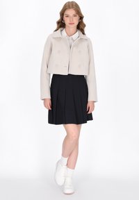 Gekürzte hellgraue Jacke mit doppelreihigen Knöpfen, kombiniert mit einem marineblauen plissierten Rock und weißen Sneakers. Glatter Stoff und taillierte Passform.