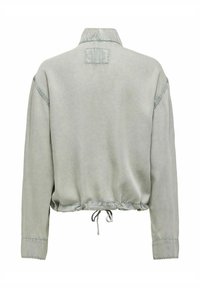 Veste gris clair à manches longues avec col montant, détail patch dans le dos, coupe ample et cordon ajustable à l’ourlet inférieur.