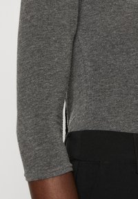 Grå långärmad skjorta med figursydd design, tillverkad av mjukt stickat tyg, kombinerad med svarta byxor med slät midjeband och texturerad yta.