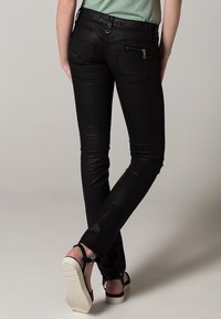 Jeans negros ajustados con una textura suave, que cuentan con un detalle de bolsillo con cremallera, bolsillos traseros estándar y un cinturón en la cintura.