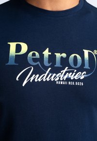 Tmavě modré bavlněné tričko s nápisem "Petrol Industries" v přechodové žluto-zelené a bílé barvě a registračním číslem vytištěným pod ním.