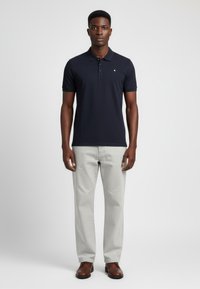 Námořnická polo košile s límečkem a krátkými rukávy, šedé kalhoty a hnědé boty. Hladká tkanina, minimální značení a přizpůsobený střih.