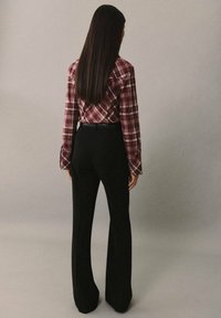 Burgundské kárované tričko s širokými rukávy, zkombinované s černými úzkými kalhotami. Oblečení je zobrazena zezadu na neutrálním pozadí.
