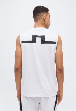 Homme de dos portant un débardeur de sport blanc avec un motif géométrique noir sur le haut du dos et un short blanc assorti.