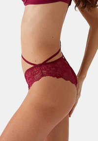 Bordeaux kant ondergoed met een bloemenpatroon, gekenmerkt door kruislings strikjes aan de zijkanten. De zachte textuur en transparante details versterken het ontwerp.